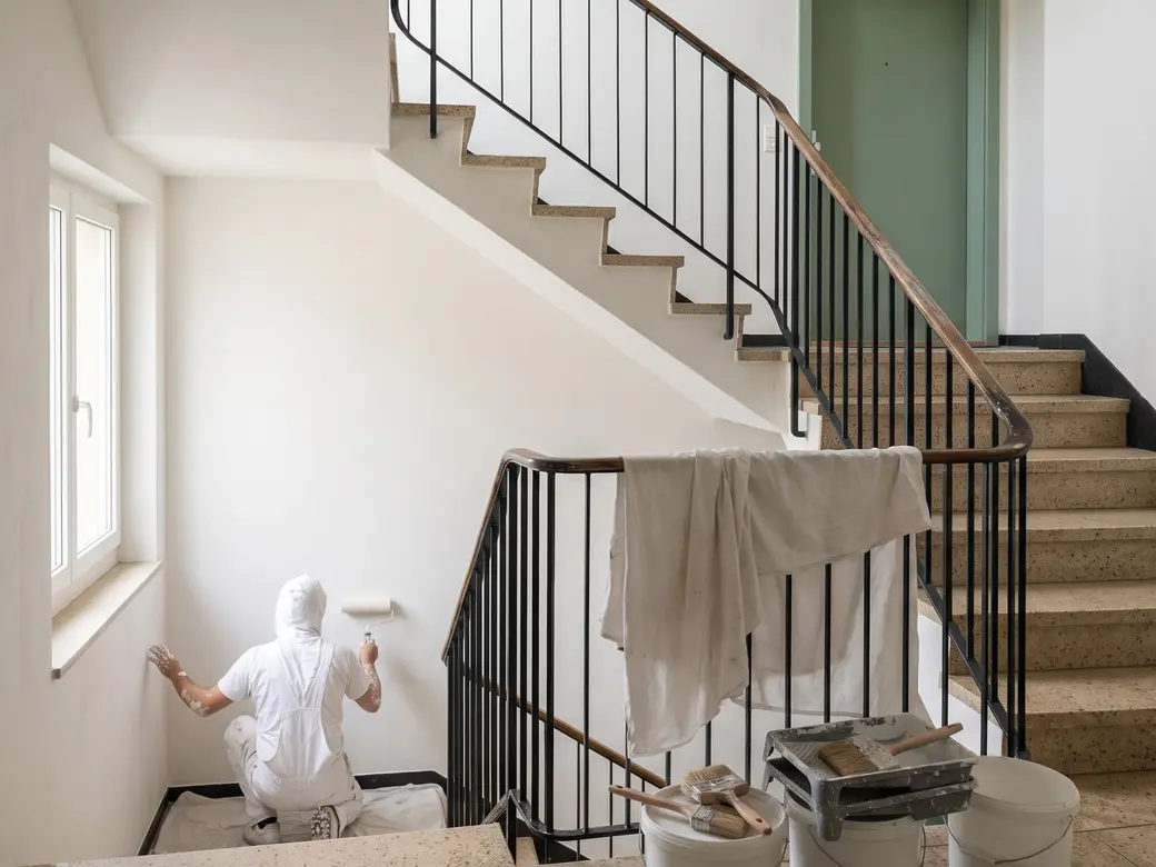 Treppenhaus eines Mehrfamilienhauses über zwei Stockwerke, helle Wände, dunkles Geländer