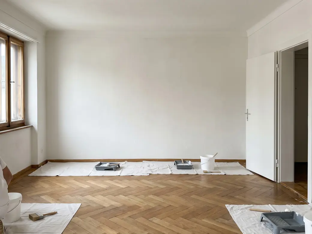 Leeres Zimmer einer Wohnung nach dem Anstrich, weisse Wände, Parkettboden, links ein Fenster