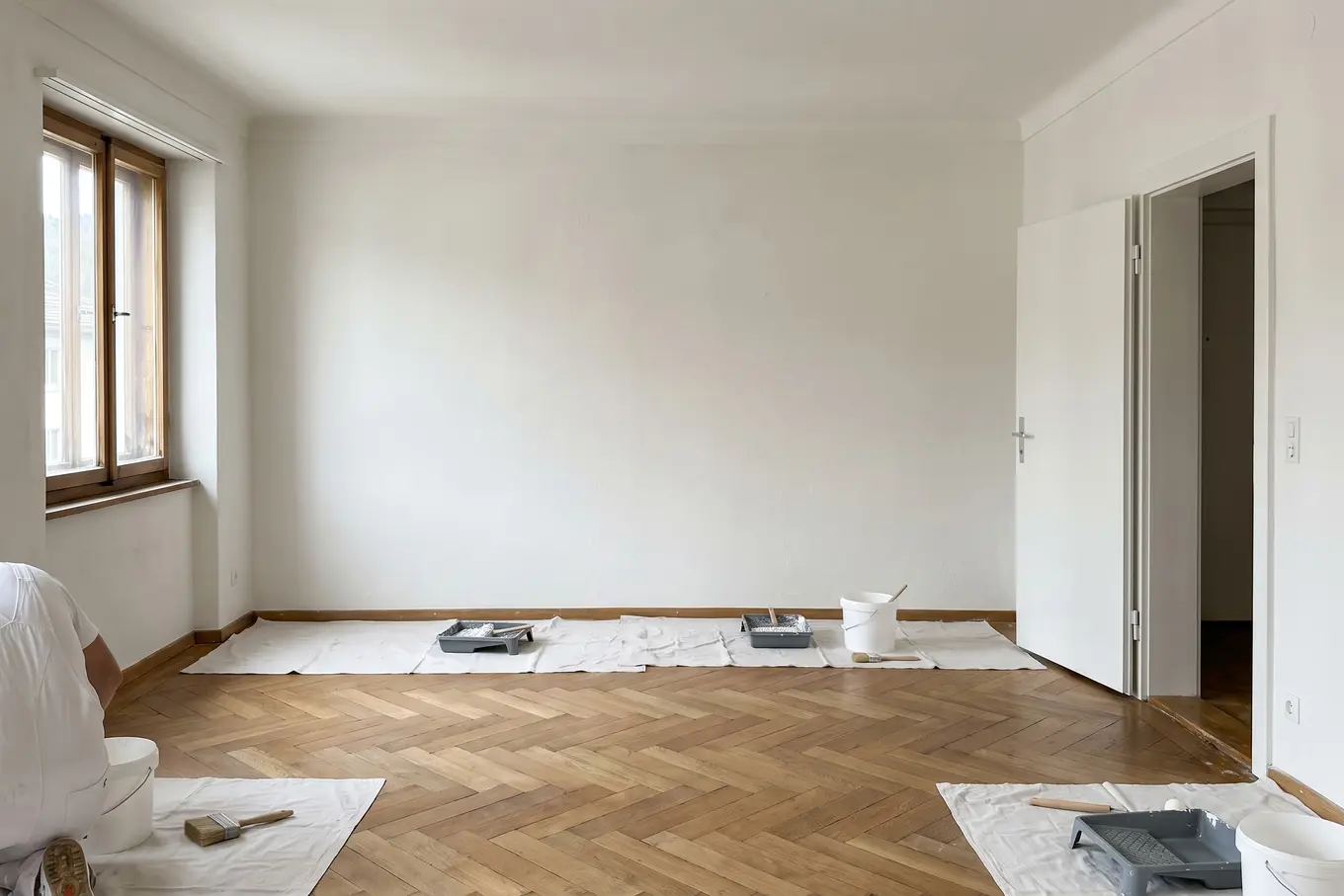 Leeres Zimmer einer Wohnung mit frisch gestrichenen weissen Wänden, Parkettboden und Abdeckvlies am Boden
